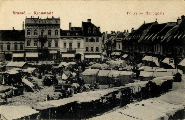 Altes Schwarz-Weiß-Foto eines belebten Marktes in Kronstadt, Deutschland, mit Menschen, Zelten und Gebäuden im Hintergrund.