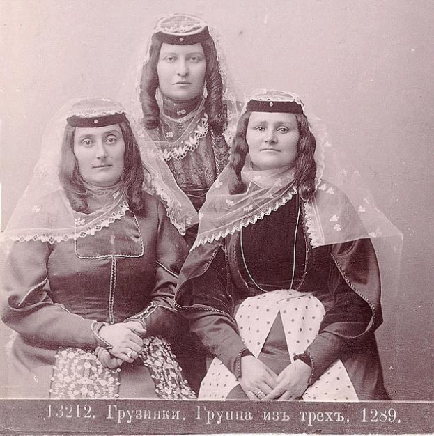 Drei Frauen in Traditionellen Russischen Hochzeitskleidern mit Farbigen Stickereien und Perlen, Posierend Gegen einer Weißen Wand in einem Schwarz-Weißen Foto.
