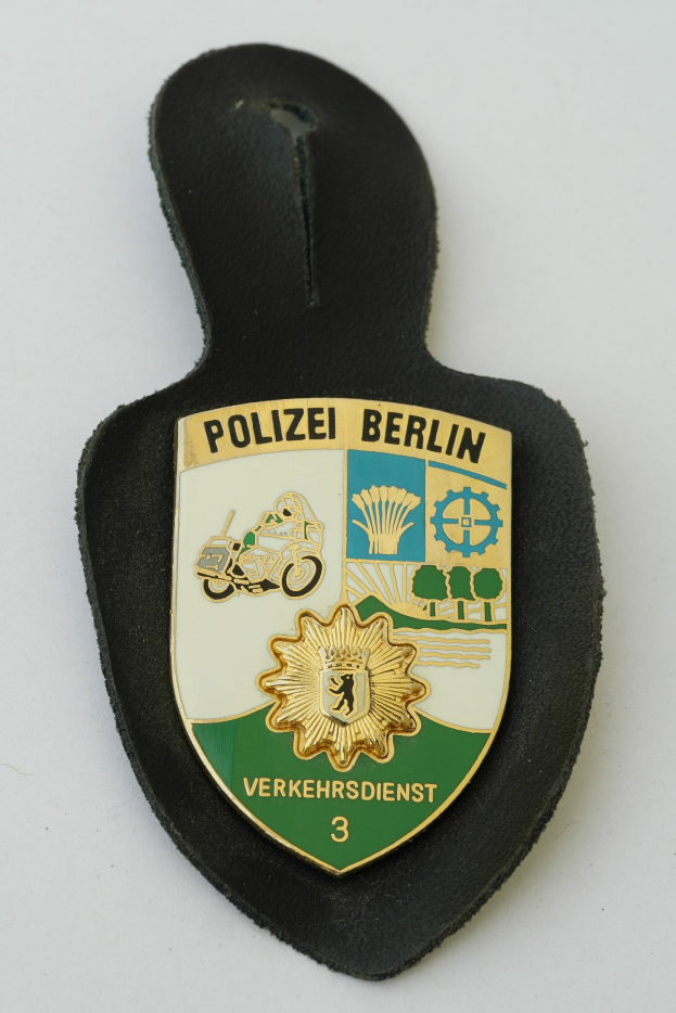 Polizei Berlin Abzeichen mit einem blauen Schild, einem weißen Stern und schwarzem Text auf einem weißen Rand, auf einer Oberfläche platziert.