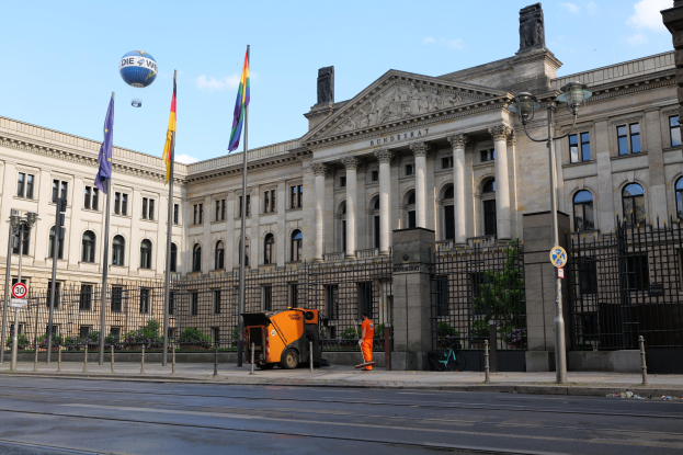 Großes modernes Gebäude mit vielen Fenstern, als Bundestag in Berlin, Deutschland identifiziert, umgeben von Straßeninfrastruktur, Fußgängern und Bäumen unter einem bewölkten Himmel.