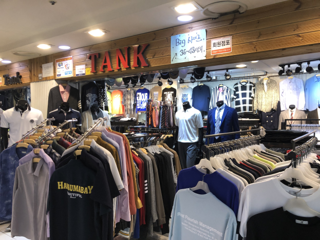 Ein Modegeschäft mit zahlreichen Shirts an der Wand, Schaufensterpuppen, die die neuesten Modetrends präsentieren, Texttafeln an den Wänden und Deckenlampen, die eine moderne und stylische Atmosphäre schaffen.