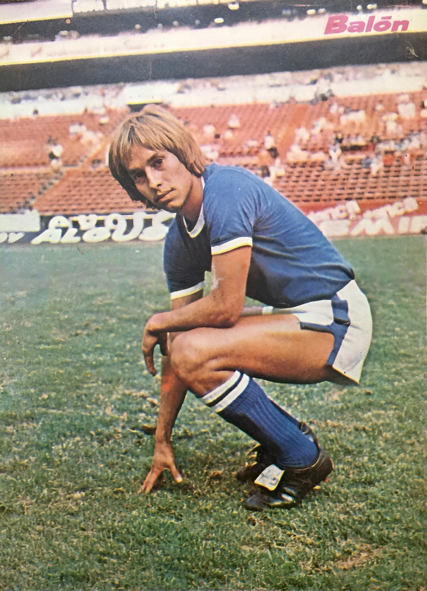 Ein Mann kniet auf einem Fußballfeld umgeben von Menschen auf Stühlen und Brettern mit Text.