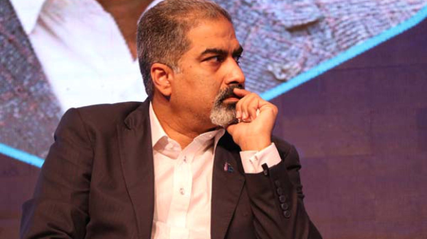 Ein Mann in Anzug und Krawatte sitzt auf einer Bühne und schaut konzentriert auf einen Bildschirm.