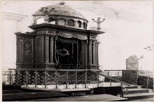 Ein altes Schwarz-Weiß-Foto einer jüdischen Synagoge in New York City, das Treppen, Geländer, Säulen, eine Tür und eine Wand zeigt, mit Text am unteren Rand: «Jüdische Synagoge in New York City».