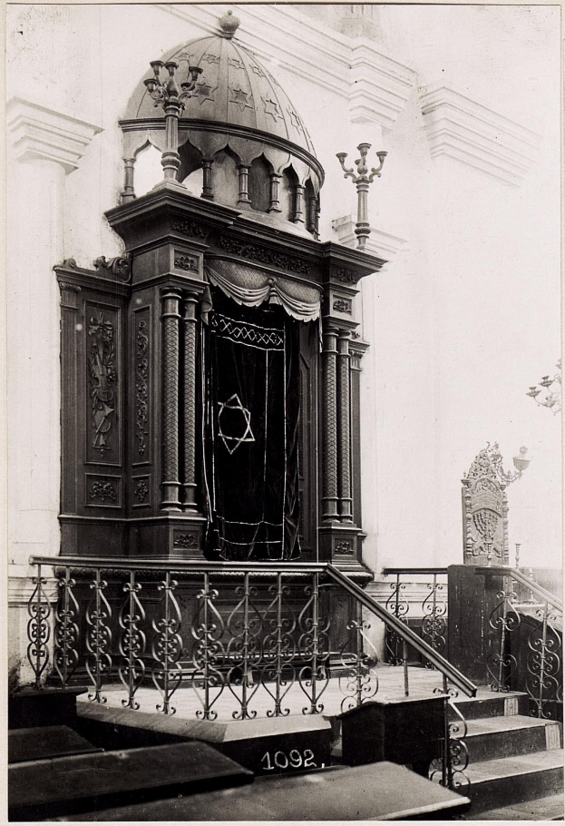 Ein altes Schwarz-Weiß-Foto einer jüdischen Synagoge in New York City, das Treppen, Geländer, Säulen, eine Tür und eine Wand zeigt, mit Text am unteren Rand: «Jüdische Synagoge in New York City».