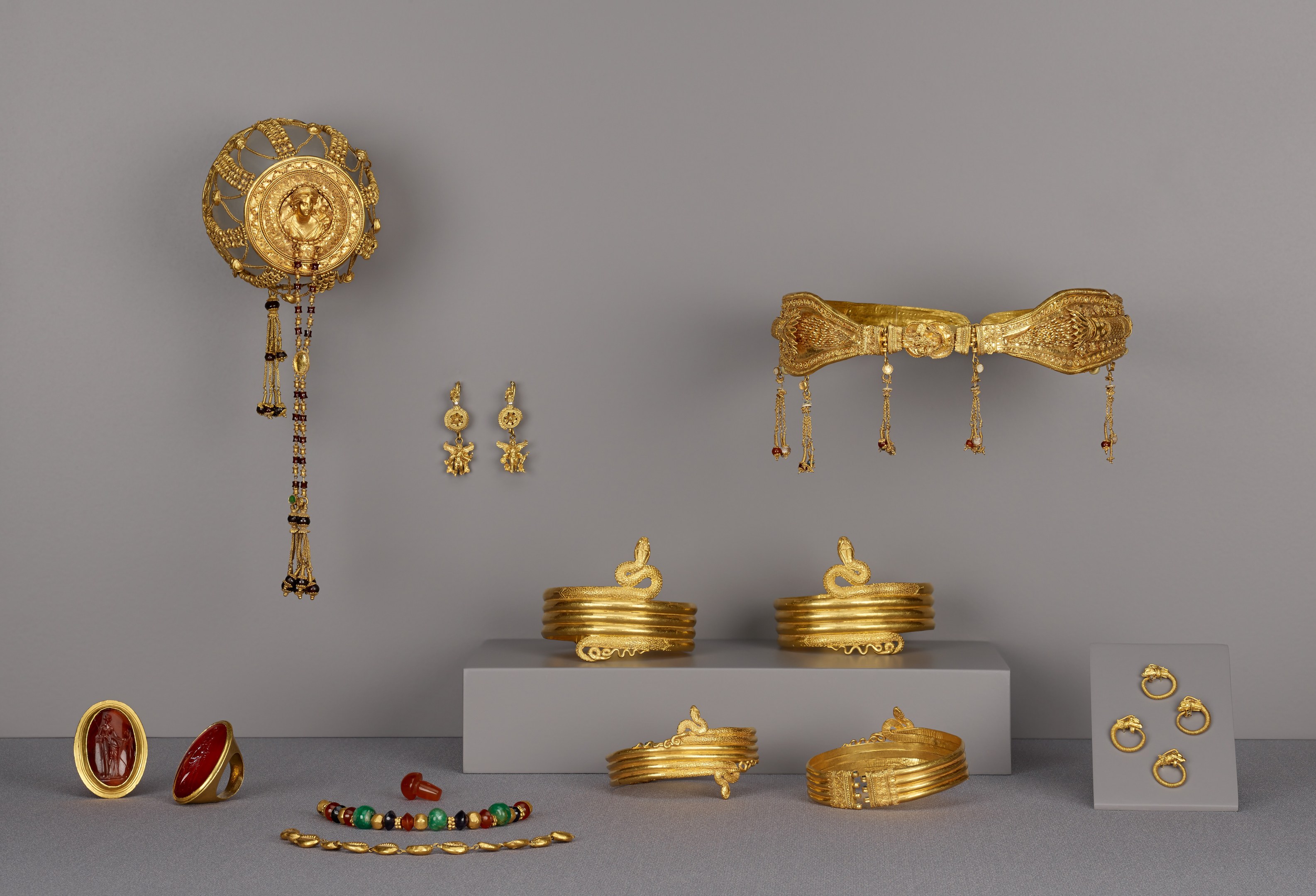 Goldschmuck-Display mit Armbändern, Ringen und anderen Stücken auf einer Oberfläche, mit zusätzlichen Stücken an der Wand im Hintergrund.
