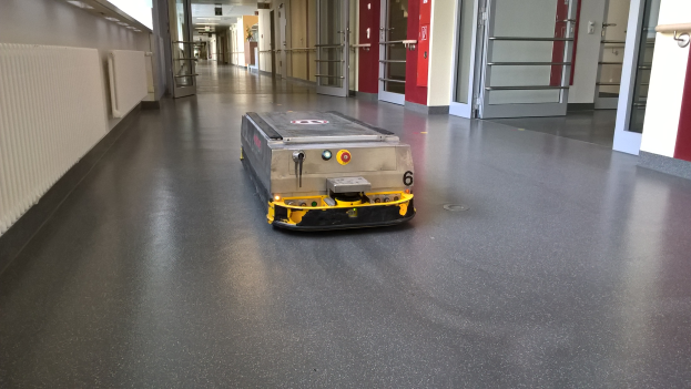 Ein Roboter, der zum Bodenreinigen entworfen wurde, steht auf dem Boden eines Gebäudes, umgeben von Wänden, Türen, Lampen und anderen Gegenständen.