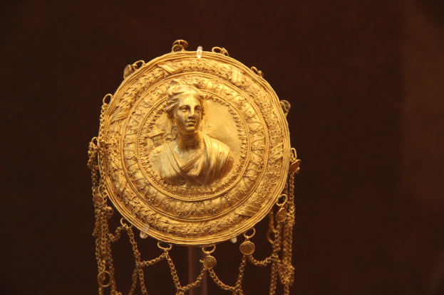 Goldene Medaille mit einer Frauengestalt auf dunklem Hintergrund, verziert mit aufwendigen Details.