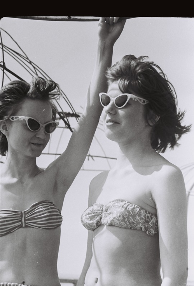 Zwei Frauen in Bikinis und Sonnenbrillen stehen Seite an Seite auf einem Schwarz-Weiß-Foto.