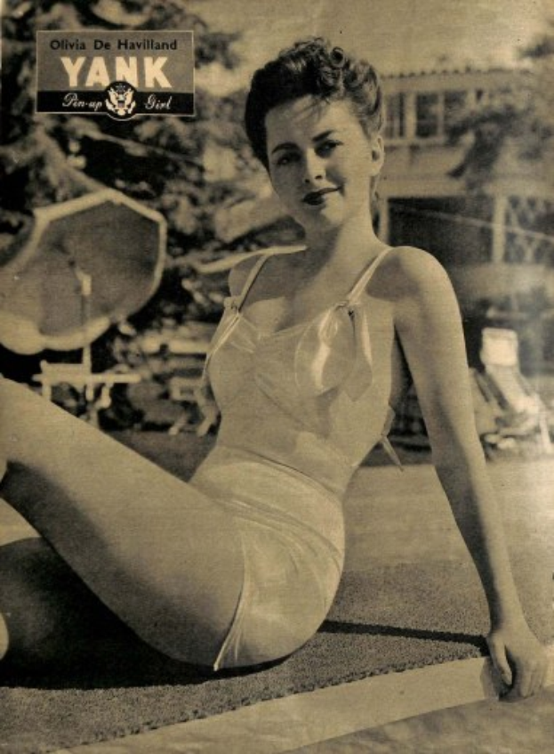 Olivia de Havilland in einem Badeanzug sitzend auf dem Boden, die lächelt, mit Bäumen, Stühlen und einem Gebäude im Hintergrund und Text oben.