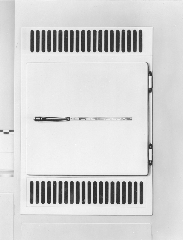 Schwarz-weiß-Foto eines rechteckigen Elektroheizgeräts mit einem Griff oben, Seitentür leicht offen, Metallrahmen und Bedienknöpfe vorne.