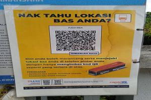 Ein Schild mit einem QR-Code, Busbild und Text vor einem Gebäude mit Bäumen und einem klaren blauen Himmel.