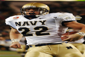 Ein Fussballspieler in einem Sportsitz und Helm läuft mit dem Ball in der Hand, Hintergrund unscharf, um Geschwindigkeit anzuzeigen.