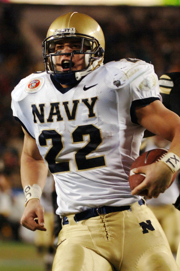 Ein Fussballspieler in einem Sportsitz und Helm läuft mit dem Ball in der Hand, Hintergrund unscharf, um Geschwindigkeit anzuzeigen.