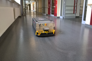 Ein Roboter, wahrscheinlich ein Reinigungsgerät, steht auf dem Boden eines Gebäudes, umgeben von Wänden, Türen, Lampen und anderen Gegenständen.