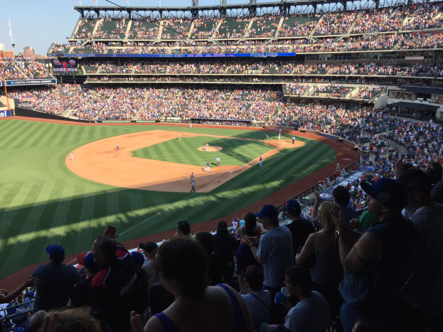 Ein Baseball-Spiel im Stadion mit Spielern auf dem Feld und Zuschauern auf den Tribünen bei strahlendem Stadionlicht.