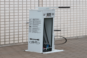 Eine Ladestation für Elektrofahrzeuge an der Seite eines Gebäudes mit einer Maschine auf dem Boden und einer Wand im Hintergrund.