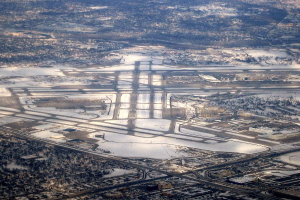 Luftaufnahme eines städtischen Flughafens umgeben von schneebedeckten Straßen, Gebäuden und Bäumen in einer winterlichen Landschaft.