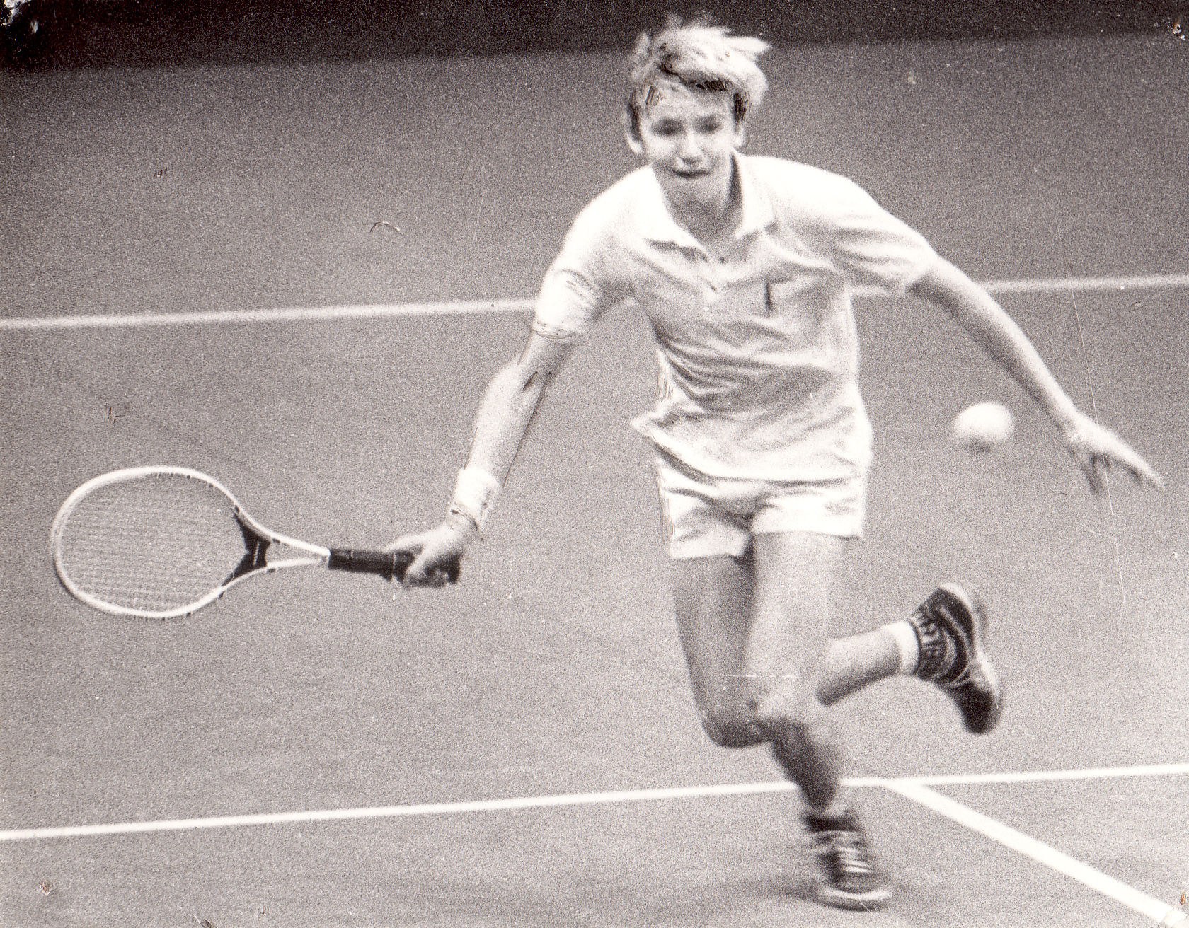 Ein junger Mann in weißer Tennisbekleidung hält einen Schläger und bereitet sich auf den Schlag eines Tennisballs auf einem Platz vor.