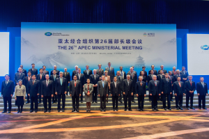 Gruppe von Menschen in formeller Kleidung auf einer Bühne mit einem Bildschirm im Hintergrund, der "Asia Pacific Economic Cooperation Summit" anzeigt.