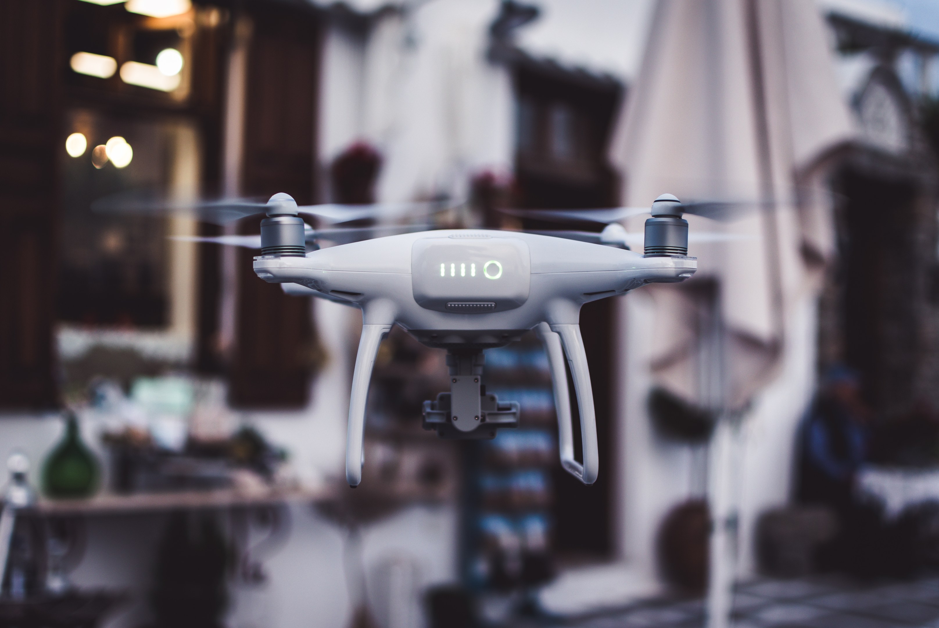 Weiße DJI Phantom 3 Advanced Drohne, die gegen einen unscharfen Hintergrund von Gebäuden und Lichtern fliegt.
