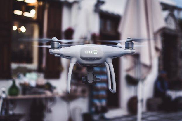 Weiße DJI Phantom 3 Advanced Drohne, die gegen einen unscharfen Hintergrund von Gebäuden und Lichtern fliegt.
