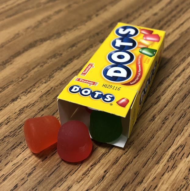 Eine Schachtel mit der Aufschrift "Pünktchen" enthält bunte Gummibärchen auf einem Holztisch.