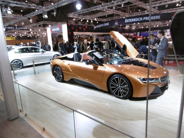 Ein elegantes schwarzes BMW i8 Roadster mit Chromakzenten auf der Frankfurter Motor Show, umgeben von formell gekleideten Gästen.