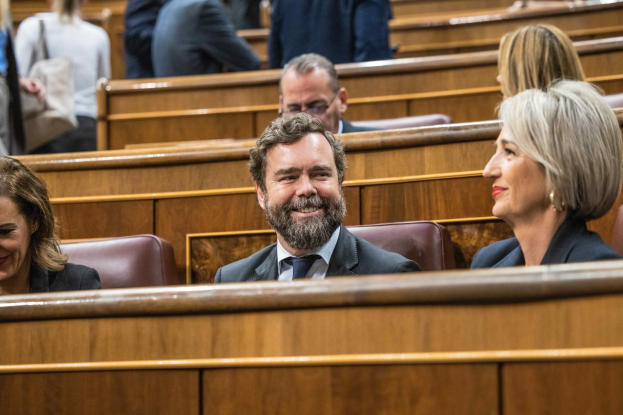 Gruppe von Menschen, die in einem Gerichtssaal sitzen, mit einem Mann in Anzug und zwei leger gekleideten Frauen, die nebeneinander sitzen und nach vorne schauen.