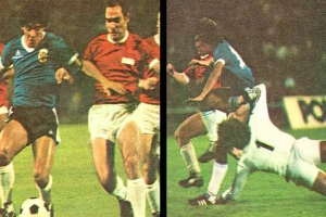 Eine Gruppe von Männern, die auf einem Feld Fußball spielen, mit einem Scoreboard im Hintergrund, ein Spieler tritt den Ball, während andere versuchen, die Kontrolle zu erlangen.