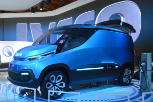Ein blauer Elektroauto auf einer Automesse ausgestellt, mit ein paar Menschen rechts daneben und einem Schild mit der Aufschrift "Iveco Concept Car" im Hintergrund.