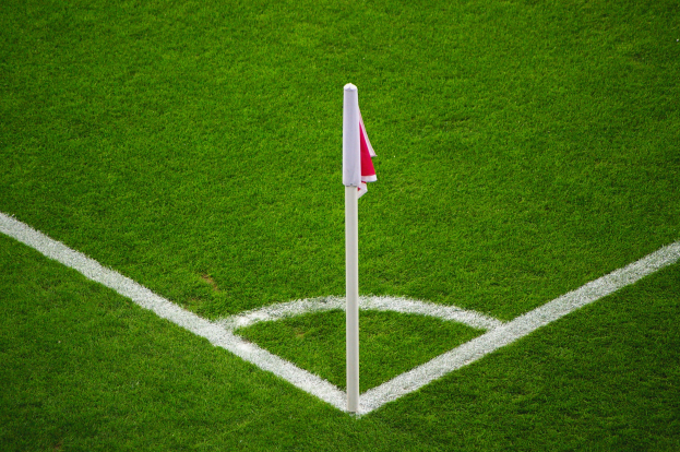 Ein Fußballfeld mit grünem Rasen, weißen Begrenzungslinien und einem weißen Pfosten mit einer roten und weißen Flagge auf dem zentralen Elfmeterpunkt.