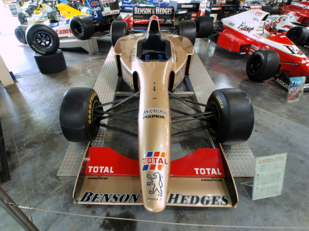 Rennwagen in einem Motorsportmuseum zu sehen, durch einen Metallzaun von Zuschauern getrennt.