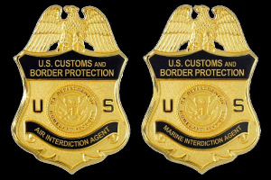 Zwei goldfarbene Abzeichen mit 'U.S. Customs and Border Protection'-Text vor einem weißen Hintergrund.