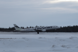 Finnair Airbus A320-200 auf einer verschneiten Landebahn am Helsinki Airport mit Bäumen und einem klaren blauen Himmel im Hintergrund.