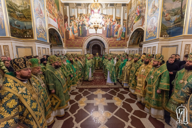 Gruppe von Priestern in grüner und goldener Kleidung, die in einer Kirche mit bemalten Wänden, einem Kronleuchter und einem Bogen im Hintergrund während einer St. Peters-Tags-Feier stehen.