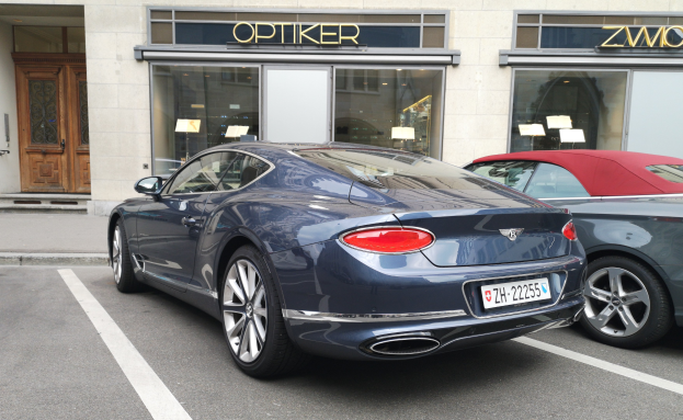 Ein schwarzer Bentley Continental GT V8 S, der auf einer Straße vor einem Gebäude mit Glaswänden und -türen geparkt ist, mit Text und Papieren auf dem Glas.