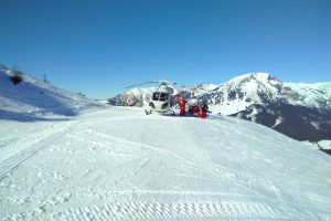 Ein Hubschrauber auf einem schneebedeckten Berg geparkt mit ein paar Menschen in der Nähe, vor einer Kulisse von schneebedeckten Bergen und Himmel.