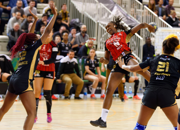 Eine Gruppe von Frauen, die Volleyball auf einem Feld spielen, während Zuschauer im Hintergrund auf Stühlen sitzen, mit Geländern und Flaschen auf dem Boden.