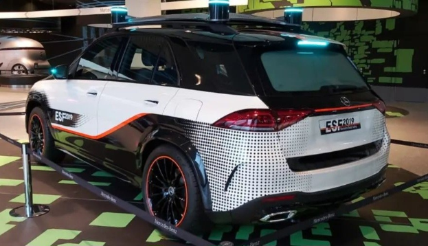 Mercedes-Benz E-Klasse Electric SUV auf der IAA in Frankfurt, umgeben von Absperrpollern mit Seilen und Lichtern, mit einem anderen Fahrzeug und Text an der Wand im Hintergrund.