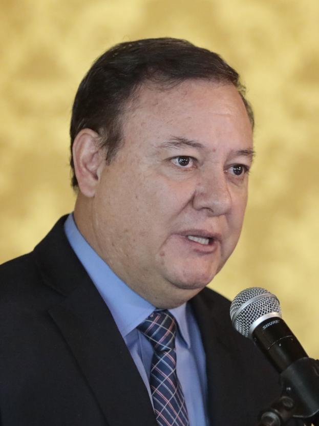 Ein Mann im Anzug mit Krawatte spricht in ein Mikrofon, identifiziert als Generalstaatsanwalt vor einem unscharfen Hintergrund.