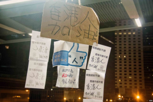 Eine Gruppe von Menschen vor einem Gebäude bei Nacht mit beleuchteten Protestschildern an der Decke.