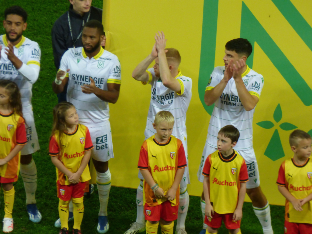 Eine Gruppe von Fußballspielern in Uniformen klatscht feierlich auf einem Ligue-1-Feld, wobei ein "Ligue-1"-Schild im Hintergrund zu sehen ist.