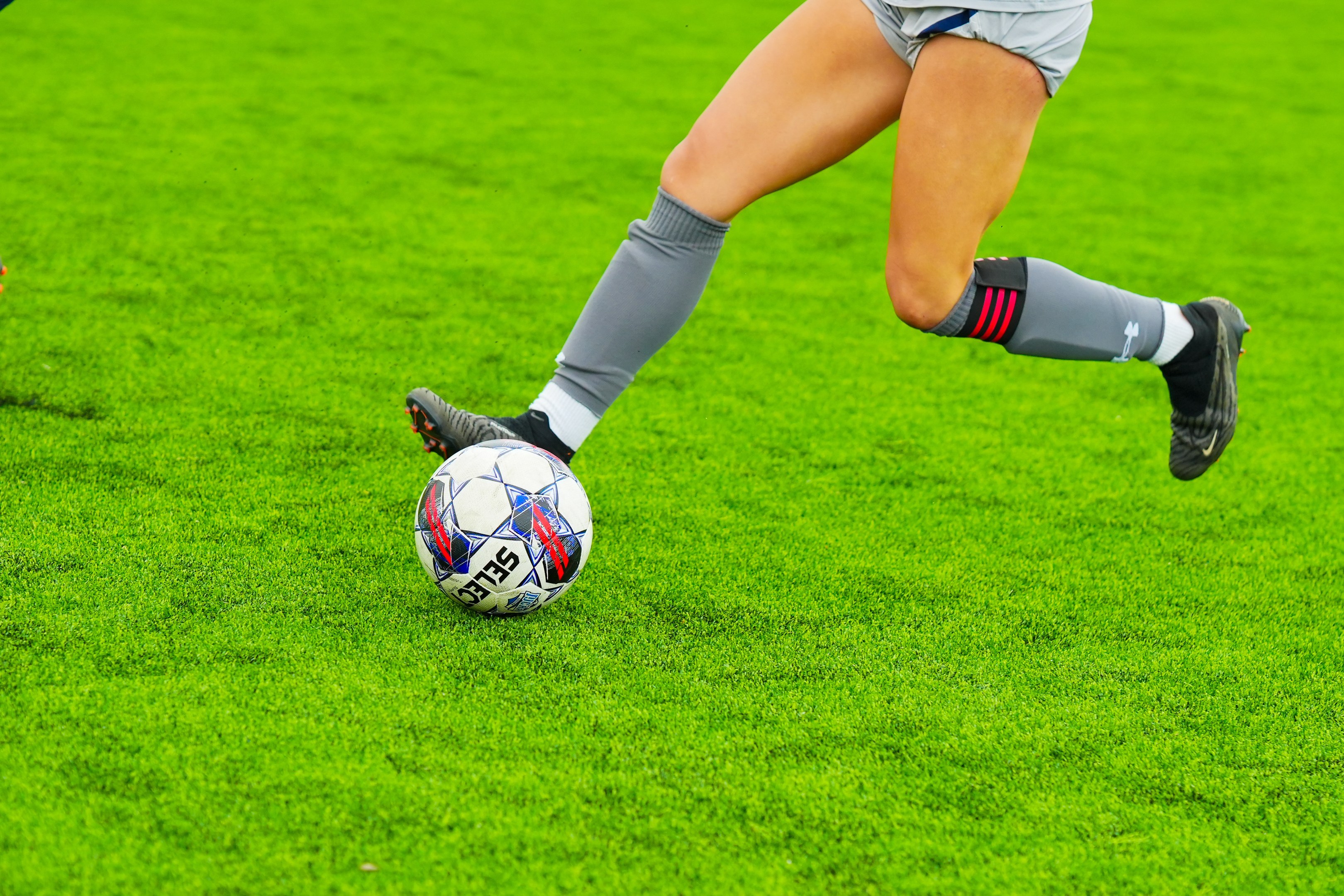 Ein professioneller Fußballspieler in einem Sportdress und -schuhen kickt einen Fußball auf einem saftigen grünen Feld.
