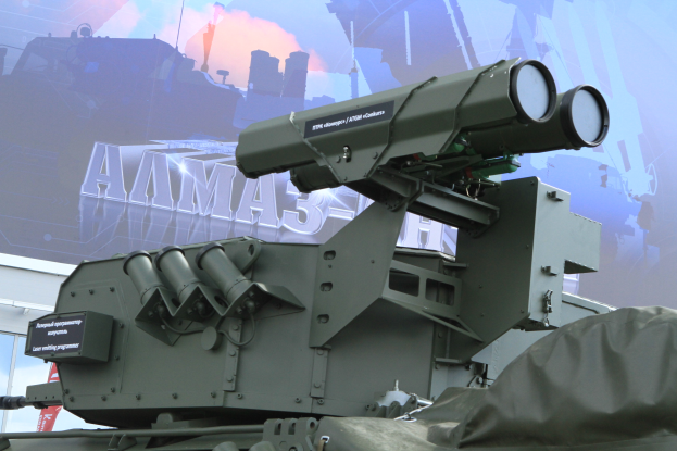 Ein militärisches Fahrzeug mit einer aufmontierten Flugabwehrrakete, das vor einem Gebäude mit einem Banner im Hintergrund geparkt ist.