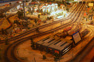 Eine detaillierte Modellbahnausstellung in einem Museum, mit Gebäuden, Bäumen, Eisenbahnschienen, Fahrzeugen, Polen, Lichtern und Tafeln, die eine belebte Stadtlandschaft nachahmen.