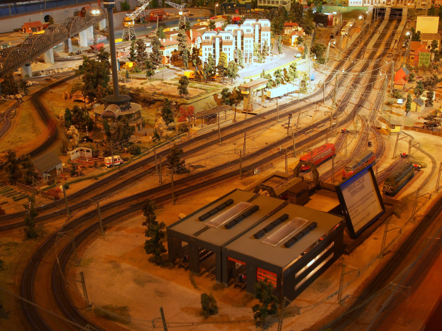 Eine detaillierte Modellbahnausstellung in einem Museum, mit Gebäuden, Bäumen, Eisenbahnschienen, Fahrzeugen, Polen, Lichtern und Tafeln, die eine belebte Stadtlandschaft nachahmen.
