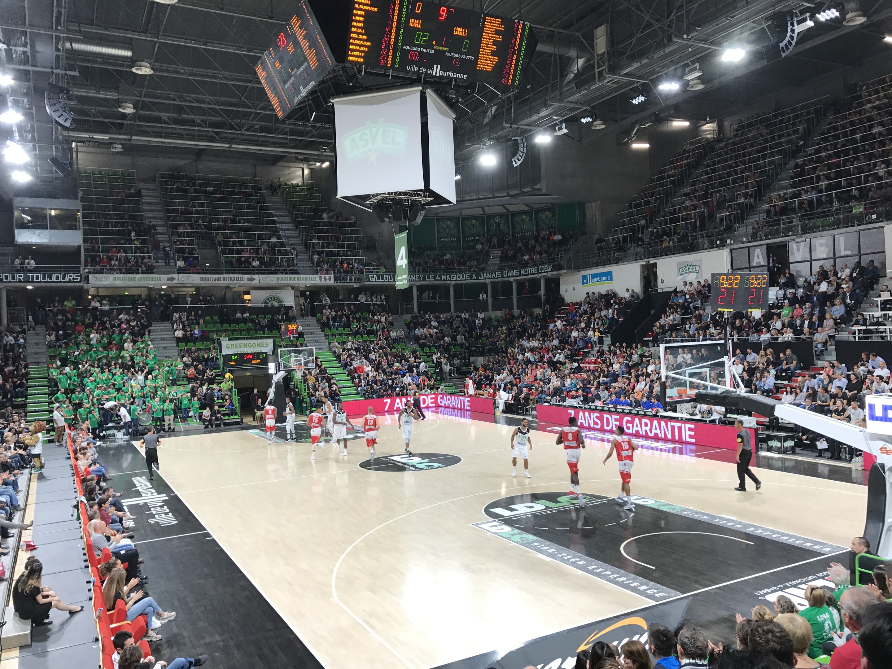 Basketballspiel in einer großen Arena mit Zuschauern, mit Beteiligung der Teams Asvel und Galatasaray, wie es die Werbetafeln am Spielfeldrand anzeigen.