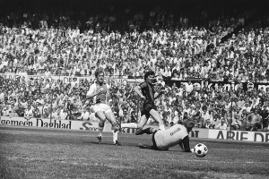 Schwarzes und weißes Foto von Männern, die auf einem Feld Fussball spielen, mit Zuschauern im Hintergrund und einem Banner mit der Aufschrift "Bundesliga 1978-79 Ajax 1-1 Hannover 96."