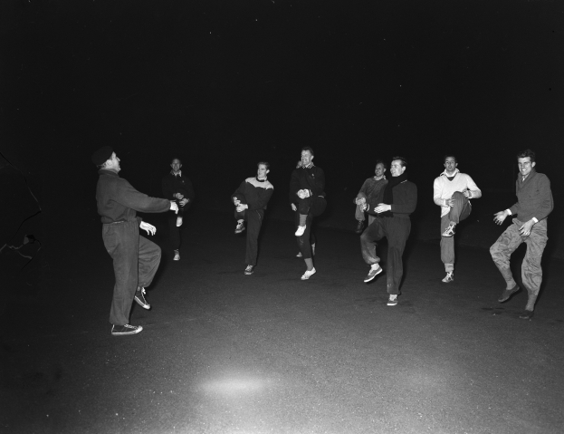 Eine Gruppe von Männern in Schuhen auf einer Bühne in einem Schwarz-Weiß-Setting, die eine Performance absolvieren.